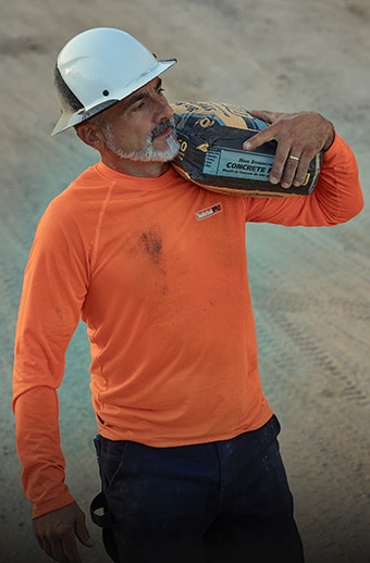 Man wearing PRO wicking shirt while carrying a bag of cement.